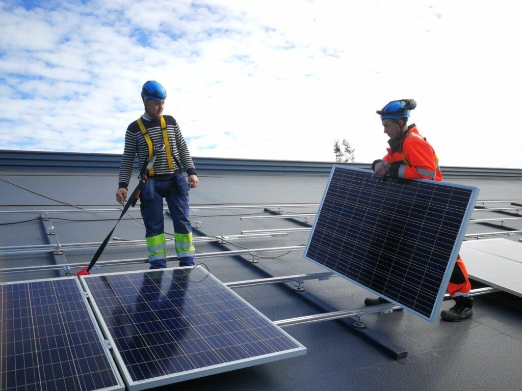 Kaksi ihmistä asentamassa aurinkopaneelia katolle.